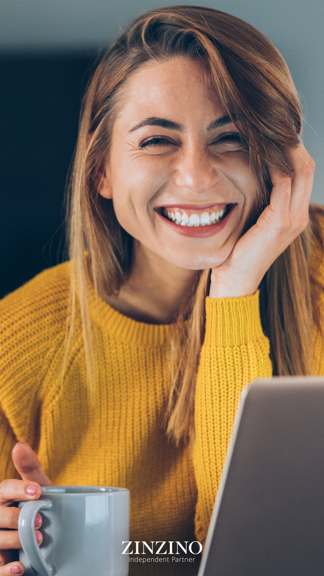Frau sitzt vor Laptop mit Kaffeetasse und lächelt. Gesundheit